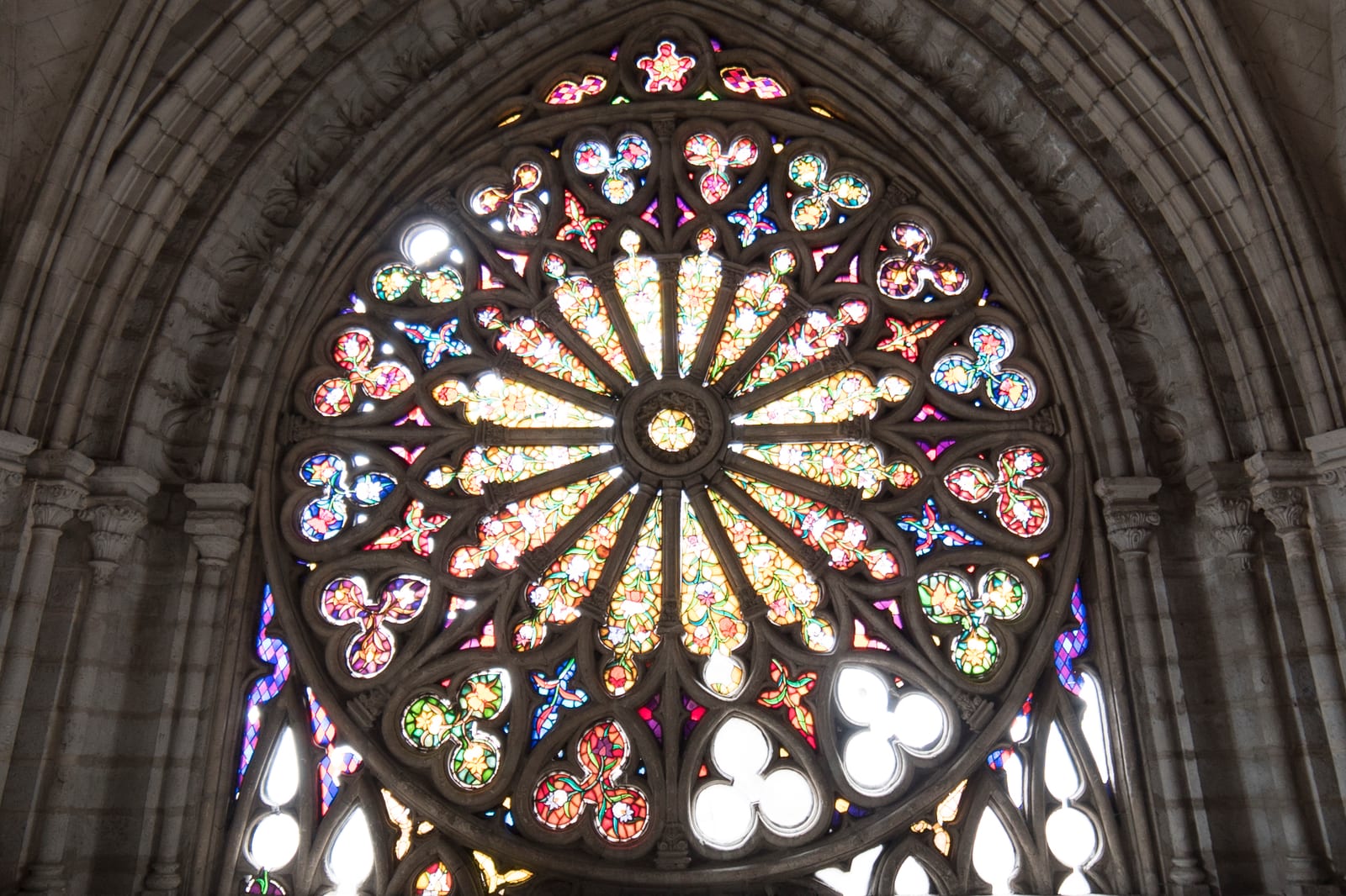 Detail of the basilica's rose window with vibrant red, blue, and yellow floral patterns set within circular Gothic tracery