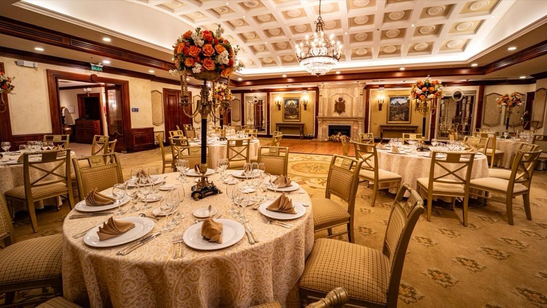 A round table at Hotel Plaza Grande with gold linens, a tall floral candelabra, fine crystal, and the ballroom's stone fireplace in the background